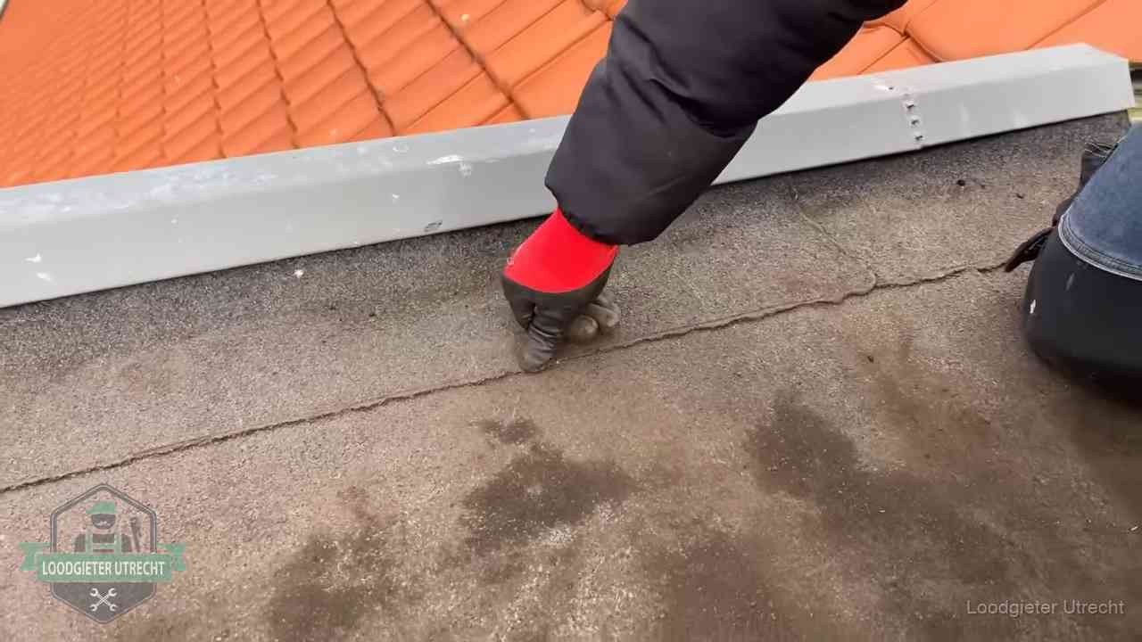Vakman wijst een naad met vochtplekken aan op een bitumen plat dak in Utrecht