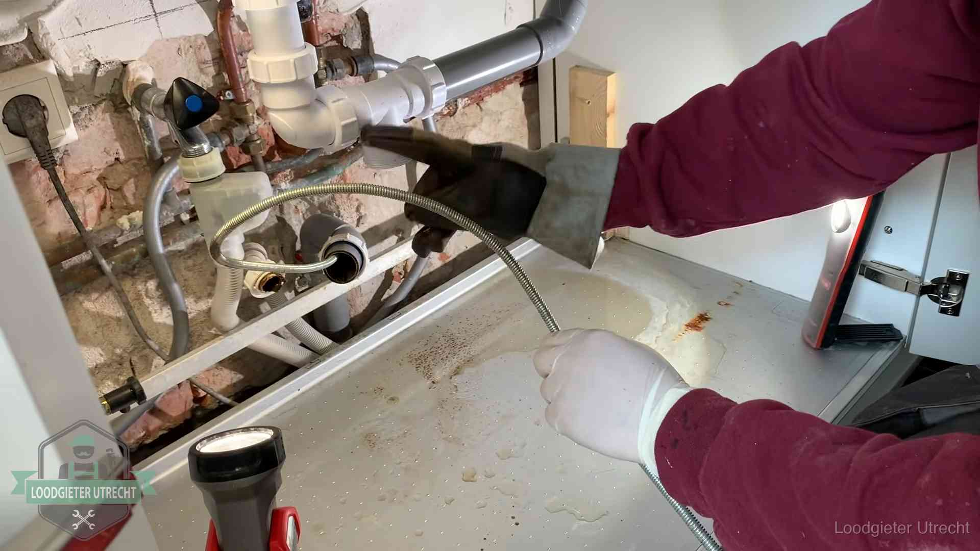 Ontstoppingsveer gaat in een geopende sifonaansluiting onder het aanrecht in Utrecht