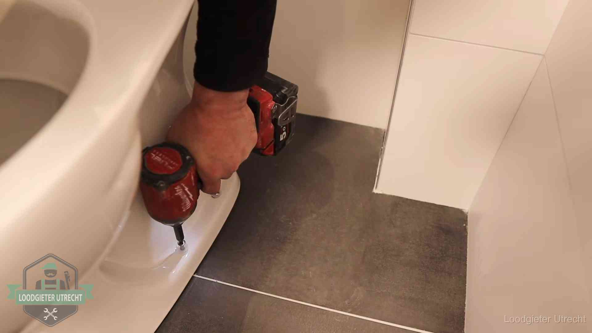 Kosten wc ontstoppen in Utrecht Loodgieter zet de voet van een wc-pot vast op de tegelvloer in Utrecht